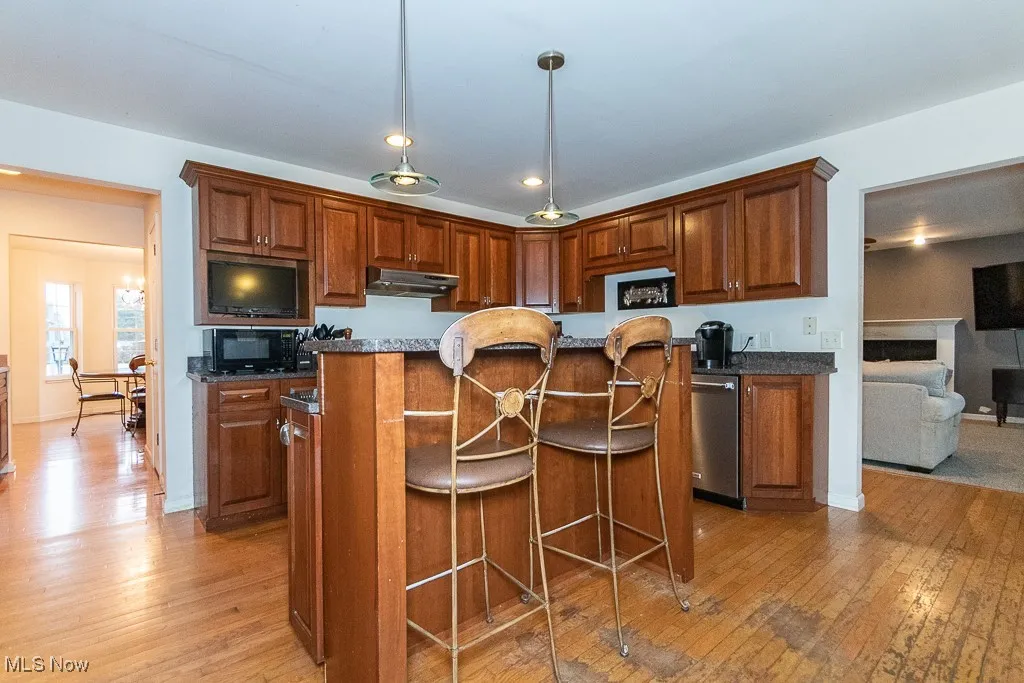 Kitchen with dark stone counters, a center island, stainless steel dishwasher, and light hardwood / wood-style flooring