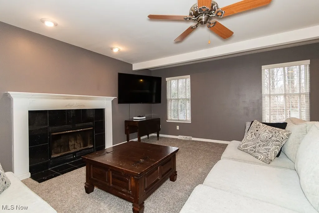 Carpeted living room featuring ceiling fan and a fireplace