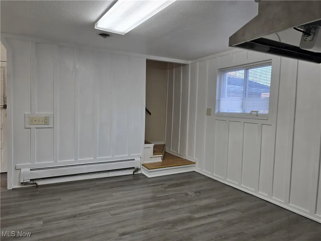 Basement with dark hardwood / wood-style floors, a textured ceiling, and baseboard heating