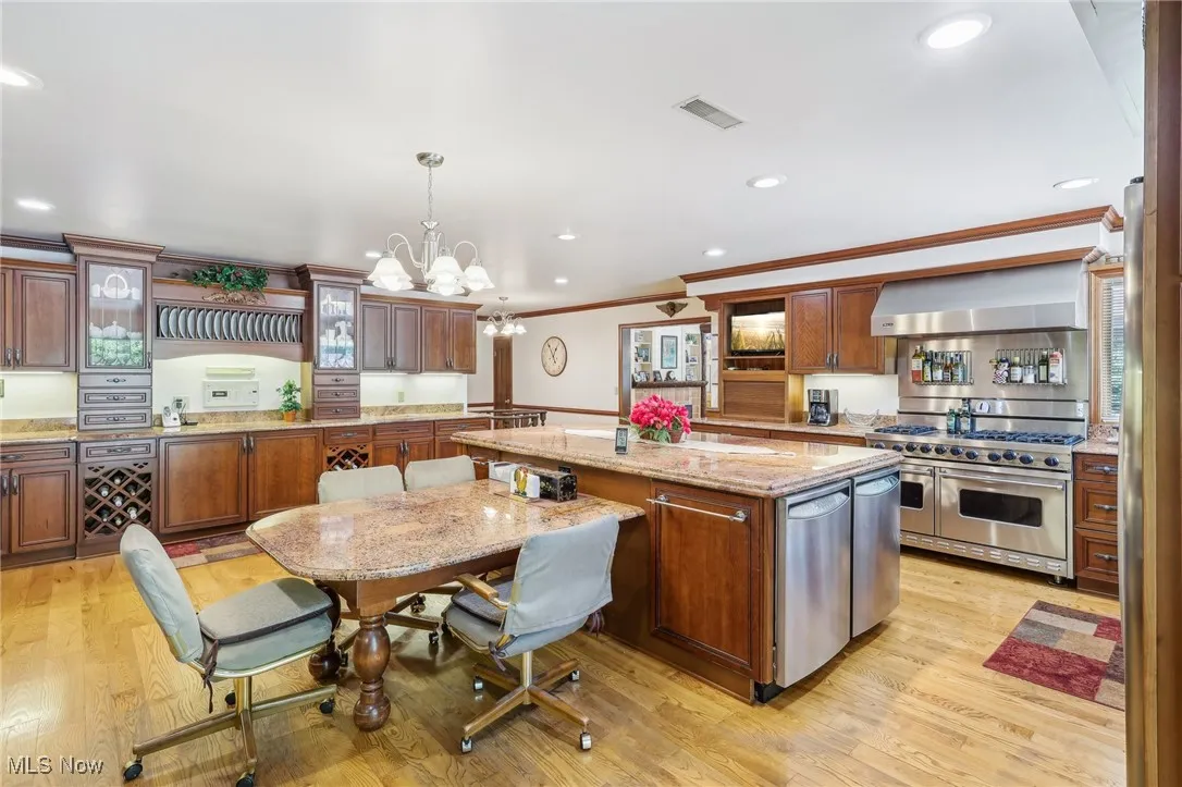 Kitchen with a center island, range with two ovens, wall chimney range hood, light hardwood flooring.