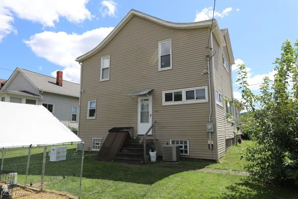 Back of the home.  This view features the back yard, outside basement access, and back door.  Also the Central A/C unit.