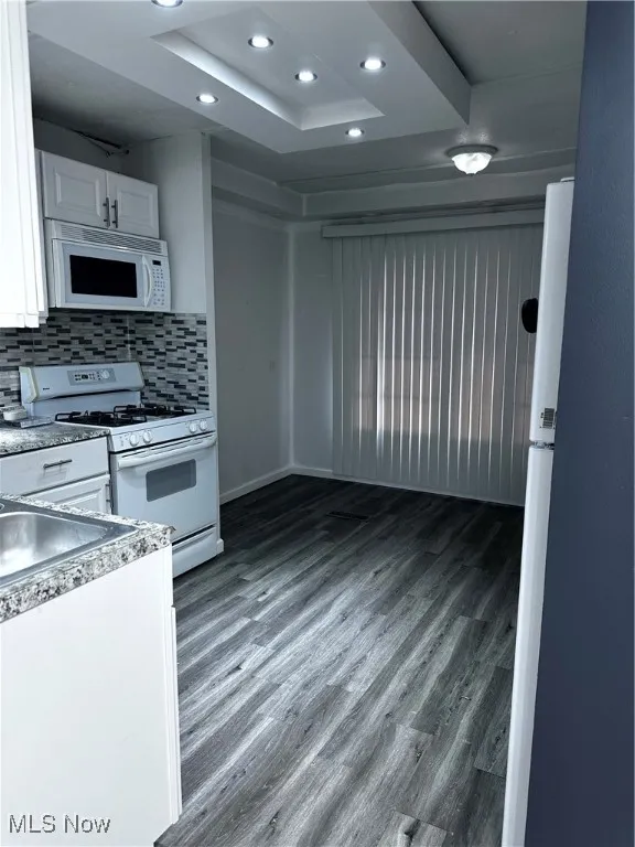 Kitchen featuring a raised ceiling, wood-type flooring, stove, decorative backsplash, and white cabinets