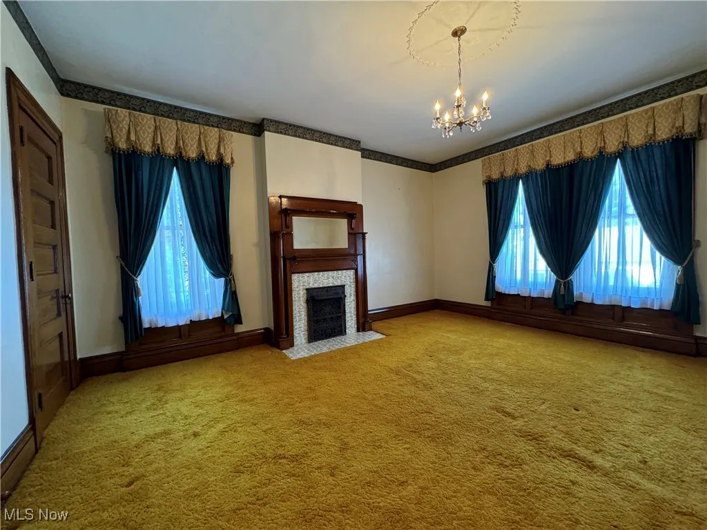 Unfurnished living room with plenty of natural light, a tiled fireplace, an inviting chandelier, and carpet floors