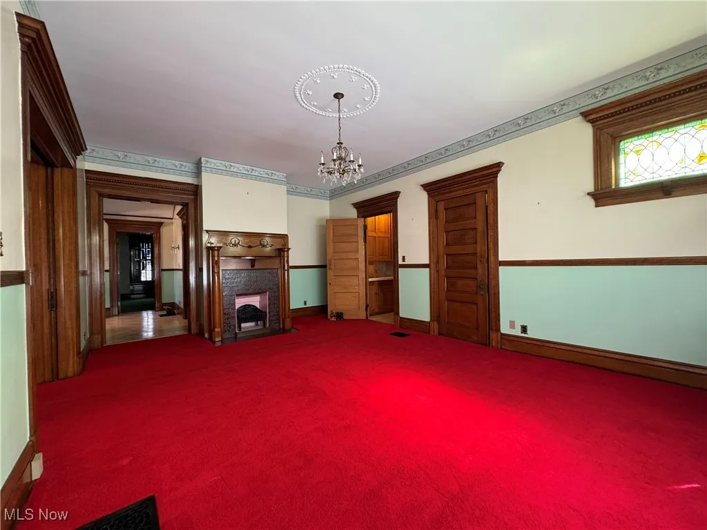 Unfurnished living room featuring dark colored carpet and a notable chandelier