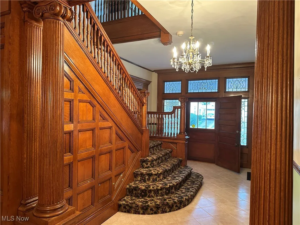 Tiled foyer featuring wood walls, an inviting chandelier, and ornamental molding