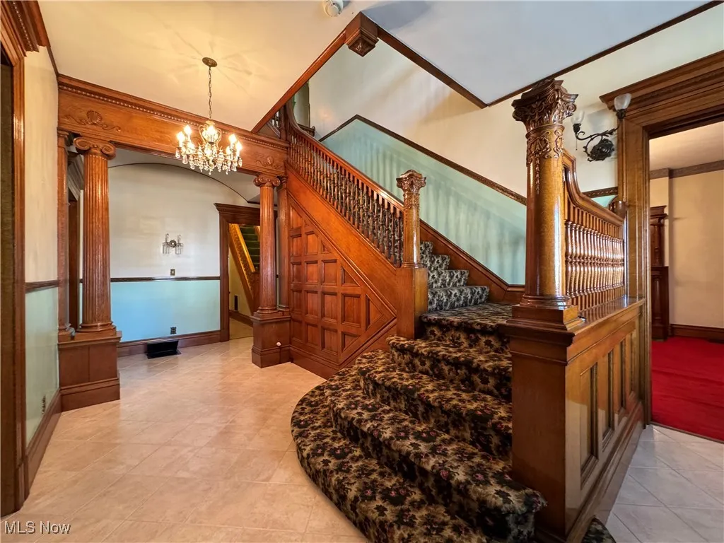 Stairway with crown molding, a notable chandelier, decorative columns, and tile patterned floors