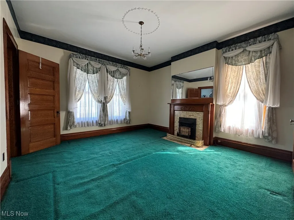 Unfurnished living room featuring a fireplace, plenty of natural light, an inviting chandelier, and carpet flooring