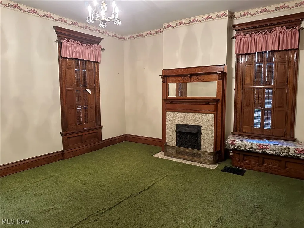 Unfurnished living room with carpet flooring, an inviting chandelier, and a stone fireplace