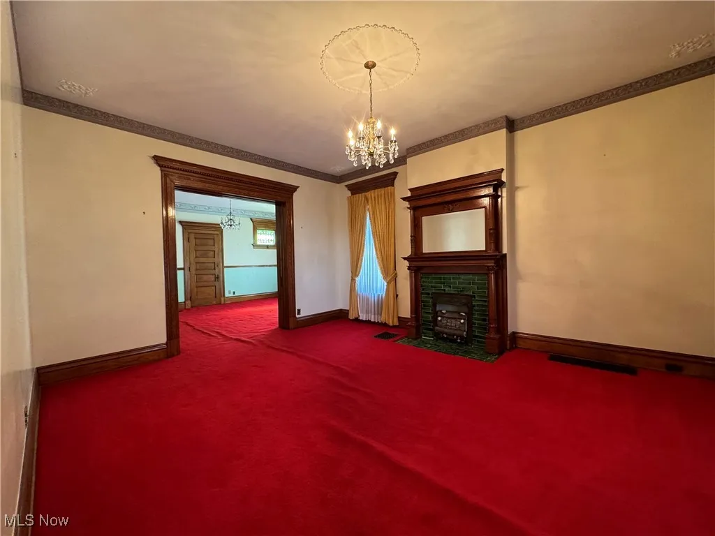 Unfurnished living room with ornamental molding, carpet flooring, and a notable chandelier
