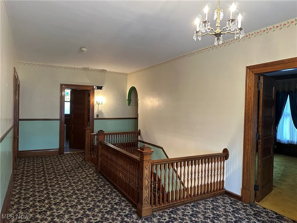 Corridor featuring plenty of natural light, dark carpet, and an inviting chandelier