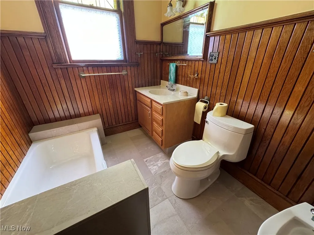 Bathroom with wood walls, toilet, a bidet, and vanity