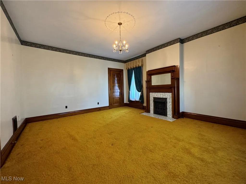 Unfurnished living room with a fireplace, crown molding, a notable chandelier, and carpet floors