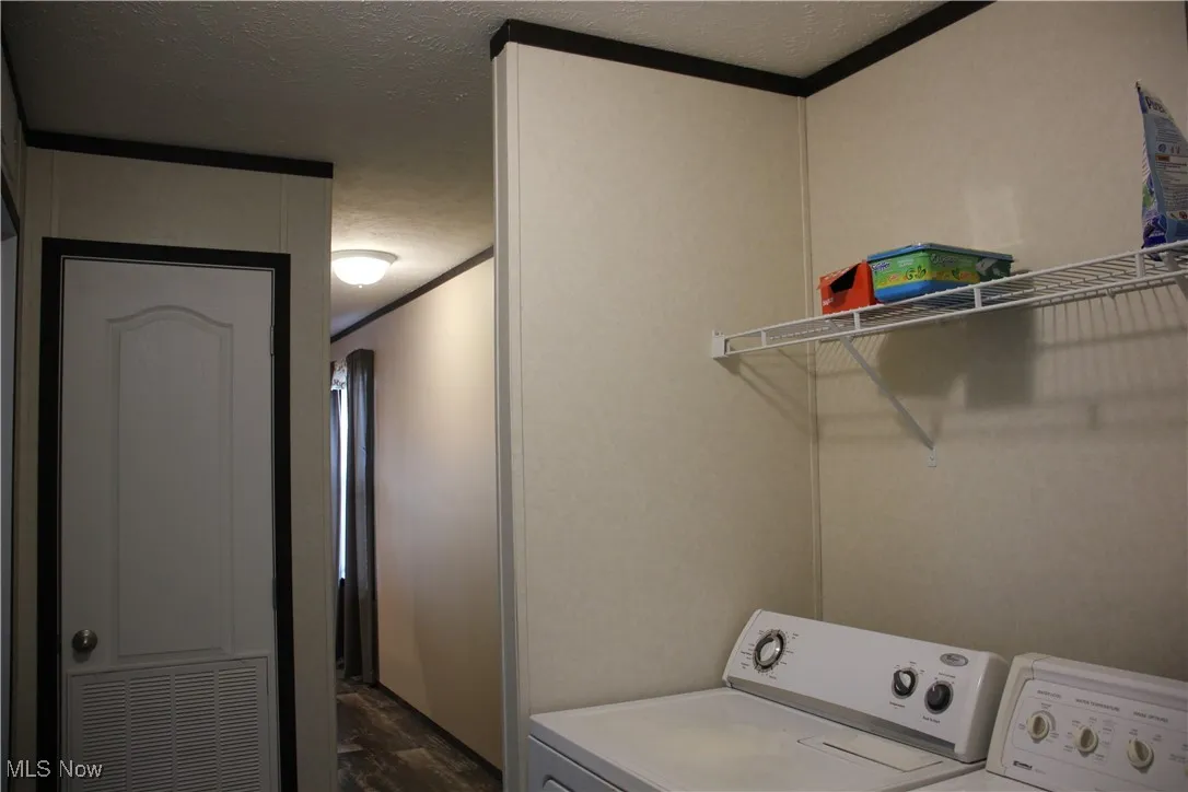 Laundry room featuring washer and dryer, crown molding, a textured ceiling, and dark wood-type flooring
