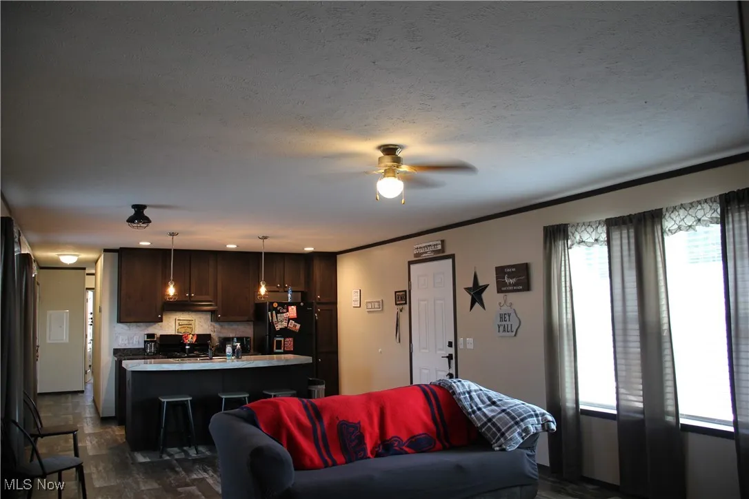 Living room with ceiling fan, ornamental molding, and a textured ceiling