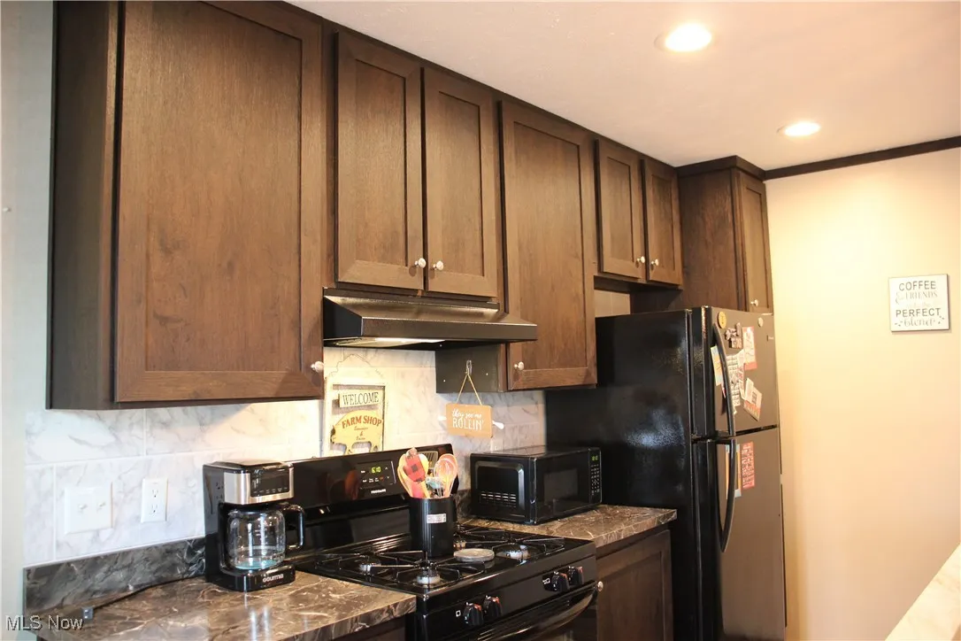 Kitchen with crown molding, black appliances, dark brown cabinets, and decorative backsplash