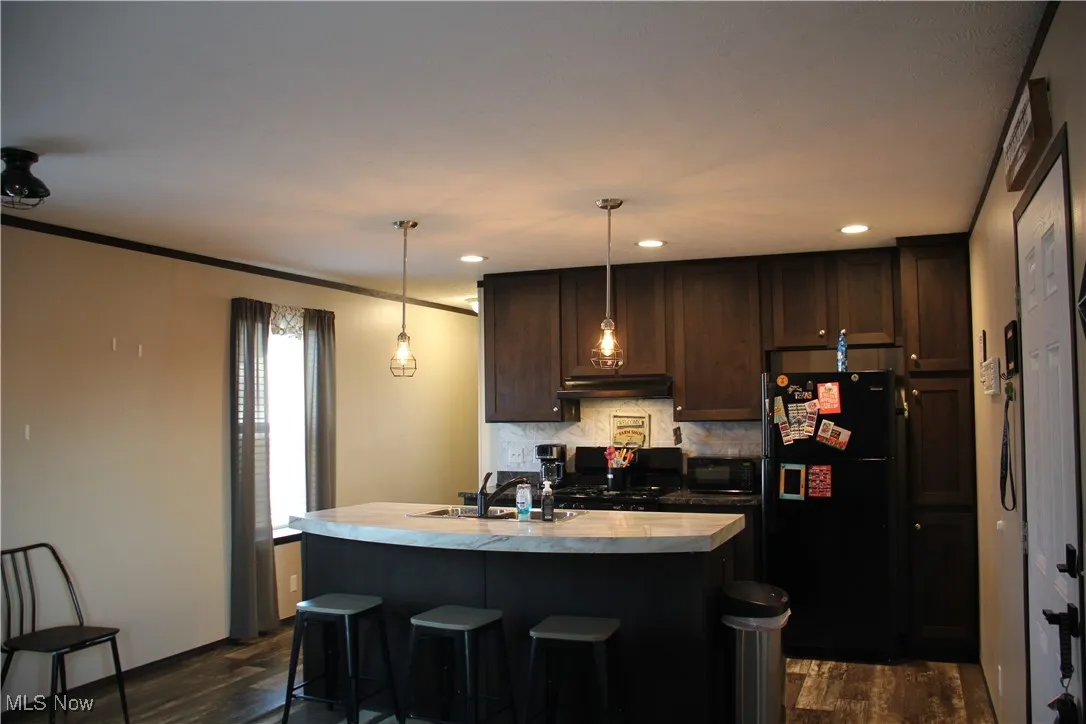 Kitchen featuring black appliances, hanging light fixtures, dark hardwood / wood-style floors, and an island with sink