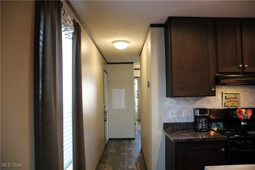 Kitchen with dark stone counters, black gas range oven, tasteful backsplash, dark brown cabinets, and dark wood-type flooring