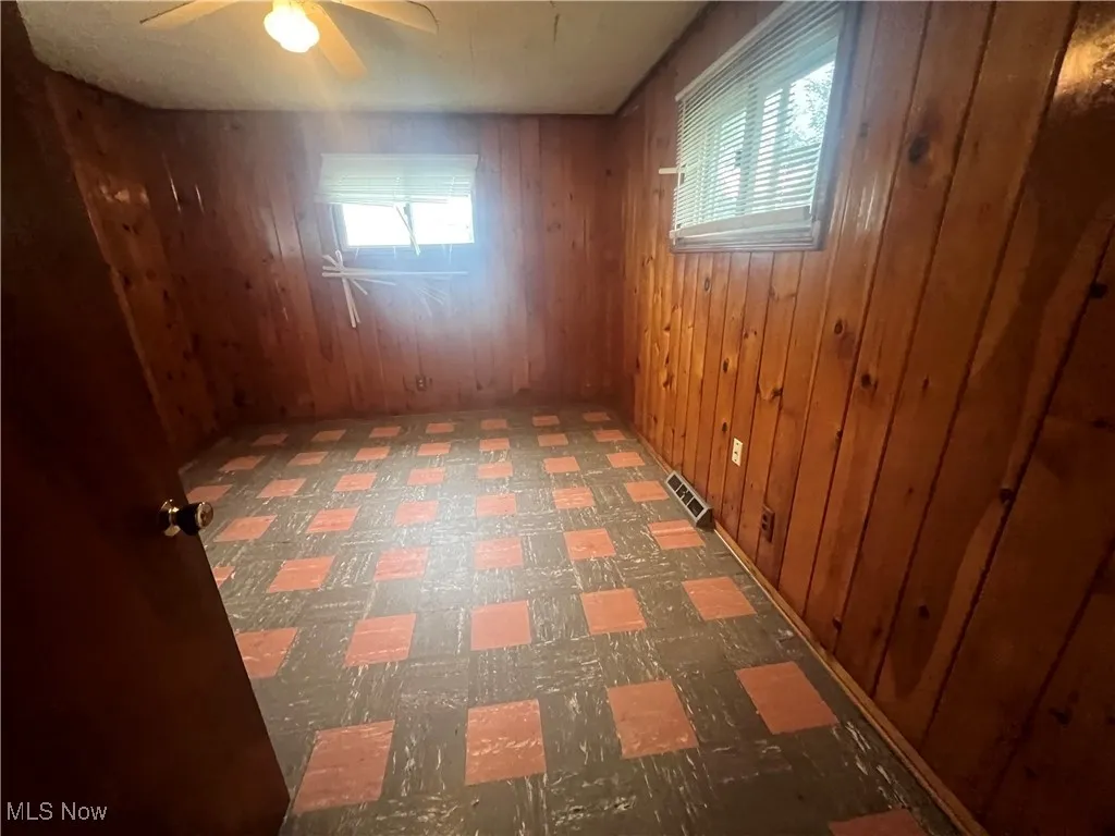 Unfurnished room featuring wooden walls and ceiling fan