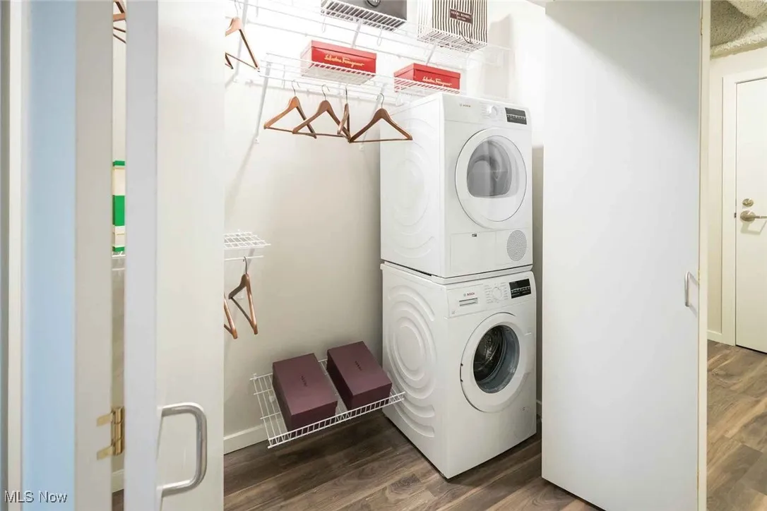 Washroom with dark hardwood / wood-style flooring and stacked washer and dryer