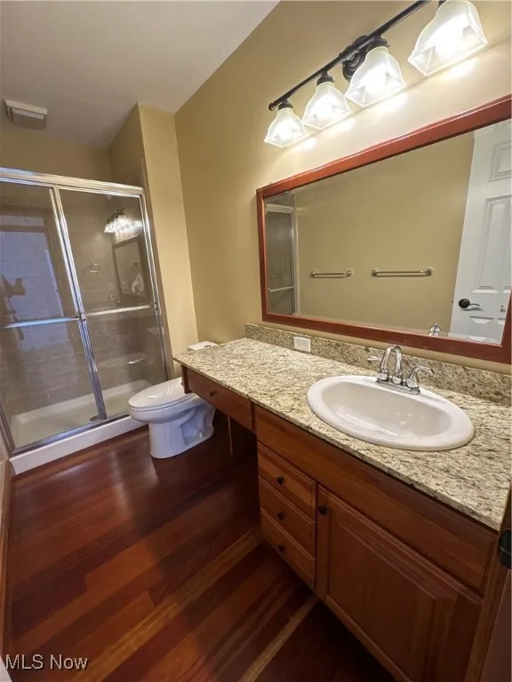 Bathroom with vanity, visible vents, wood finished floors, toilet, and a stall shower