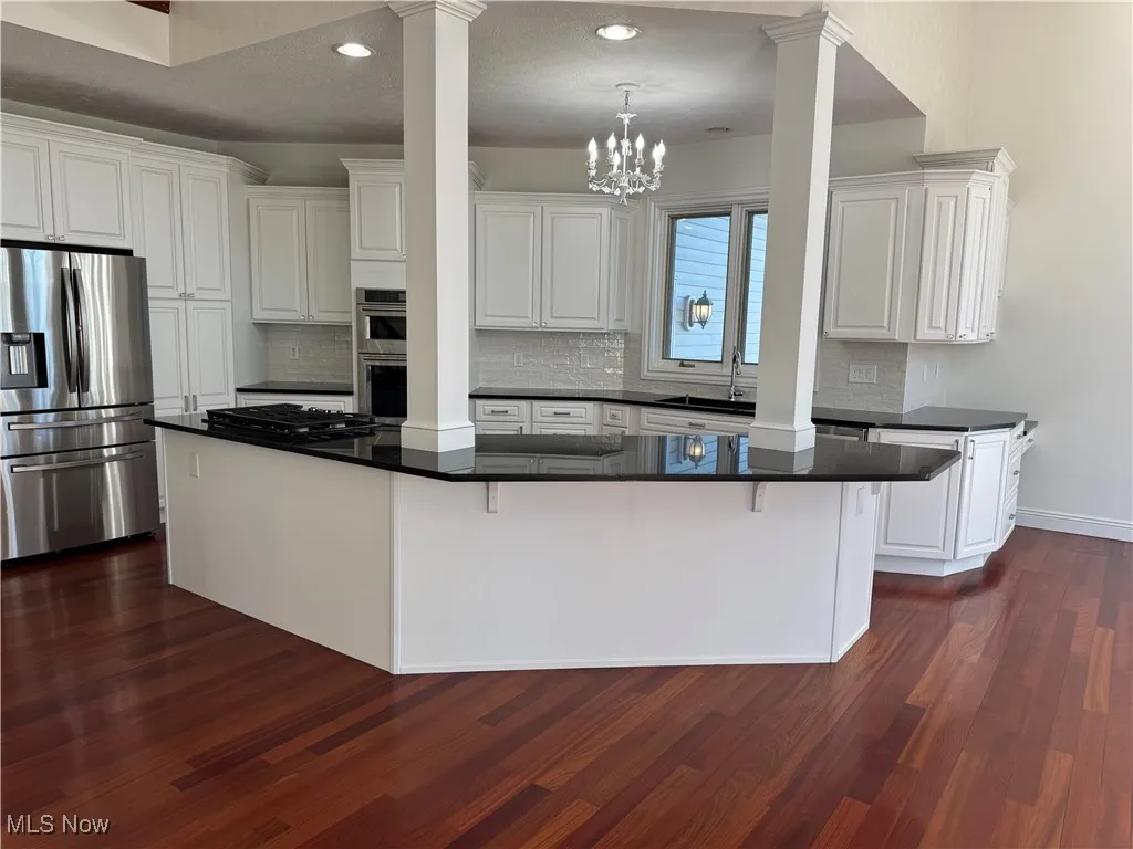 Kitchen with decorative columns, dark countertops, appliances with stainless steel finishes, and dark wood-type flooring