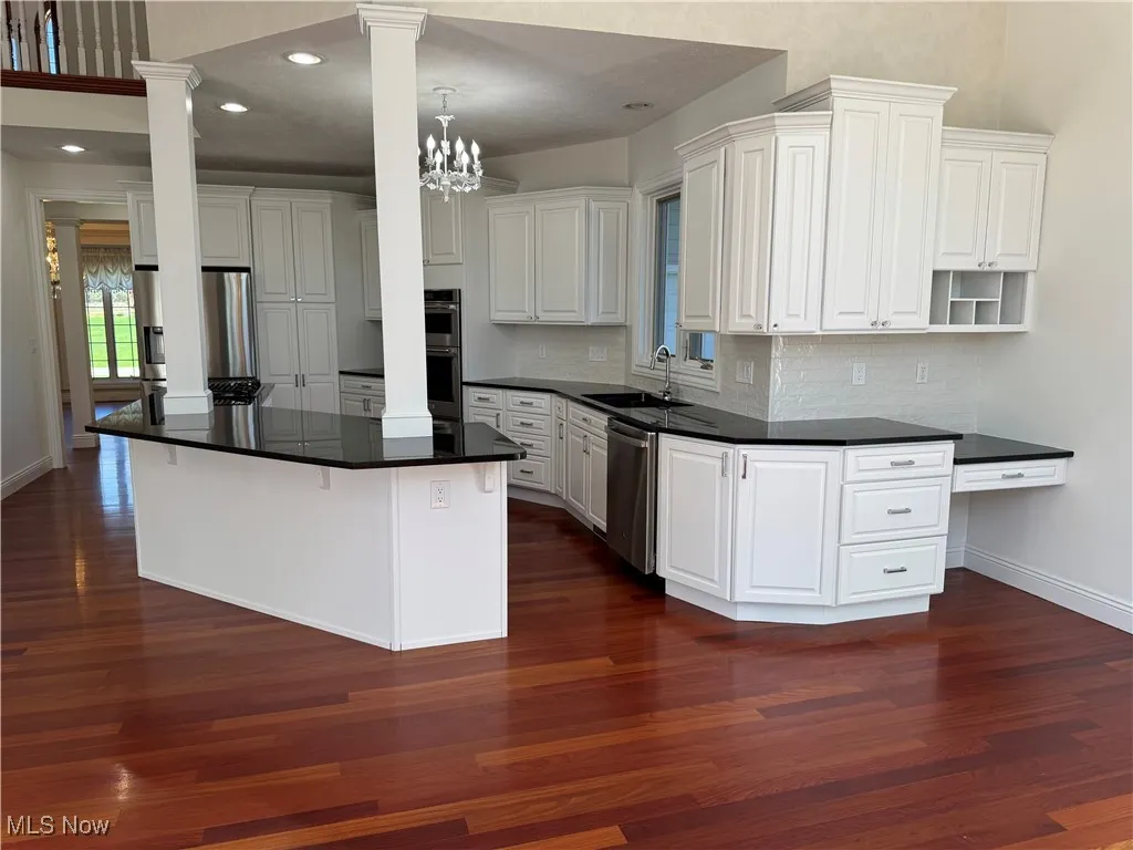 Kitchen featuring decorative columns, tasteful backsplash, a sink, dark wood finished floors, and stainless steel appliances