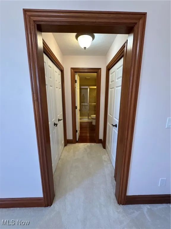 Corridor featuring light colored carpet and baseboards