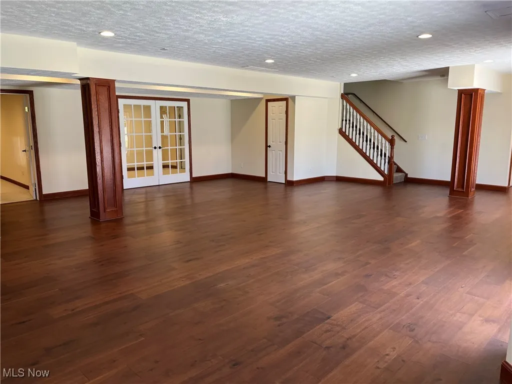 Unfurnished living room featuring french doors, stairs, baseboards, and dark wood-style floors