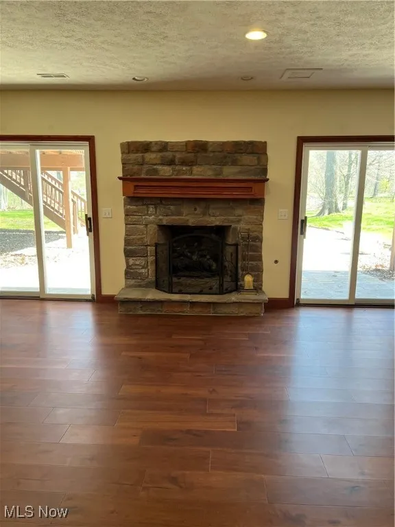 Unfurnished living room with baseboards, a stone fireplace, a textured ceiling, and wood finished floors