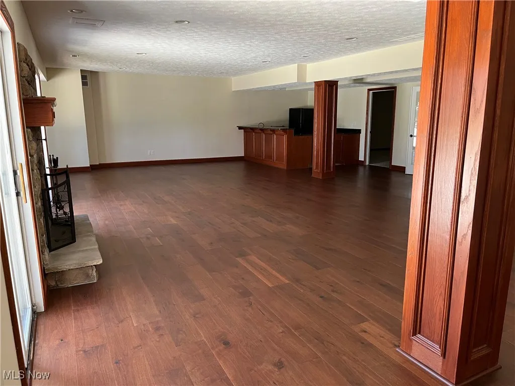 Unfurnished living room with baseboards, dark wood-style floors, and a textured ceiling