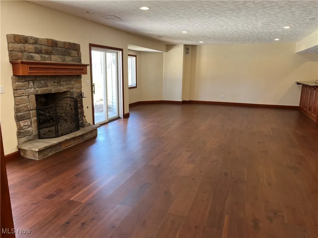 Unfurnished living room with dark wood-style flooring, a textured ceiling, a stone fireplace, recessed lighting, and baseboards