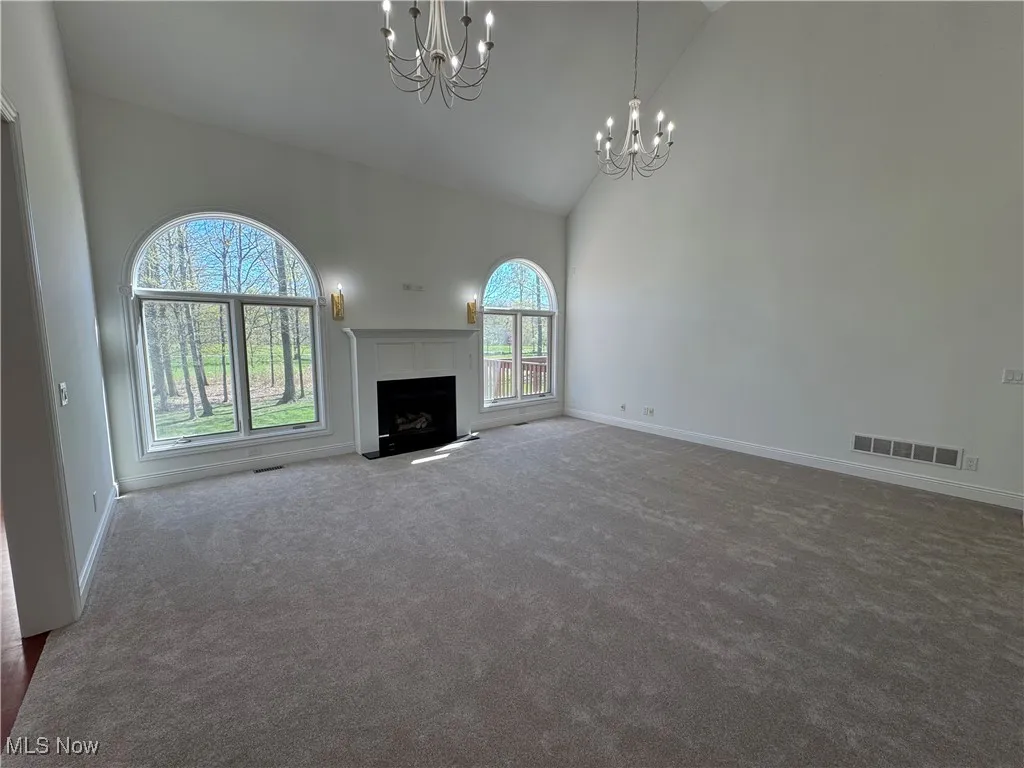 Unfurnished living room with a notable chandelier, carpet floors, high vaulted ceiling, baseboards, and visible vents