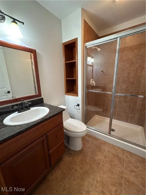 Full bathroom featuring vanity, toilet, tile patterned floors, and a stall shower