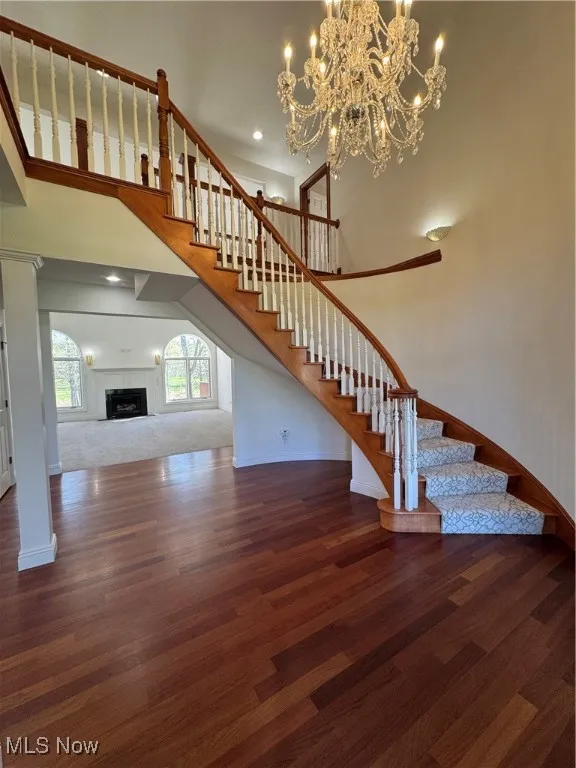 Unfurnished living room featuring stairway, baseboards, wood finished floors, and a notable chandelier