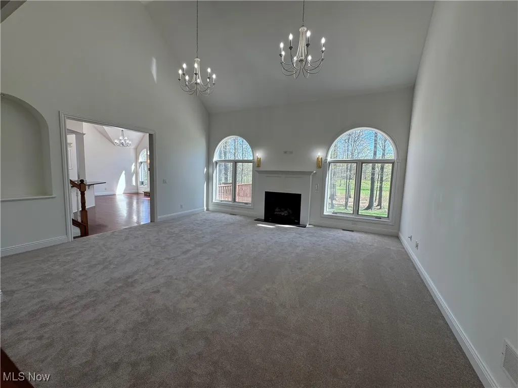 Unfurnished living room with high vaulted ceiling, a chandelier, plenty of natural light, and carpet