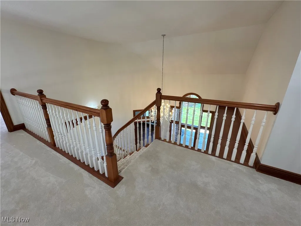 Stairway featuring baseboards, carpet, lofted ceiling, and a notable chandelier