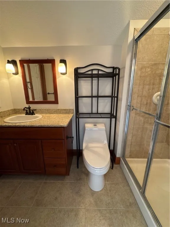 Bathroom with toilet, a shower stall, tile patterned flooring, and vanity