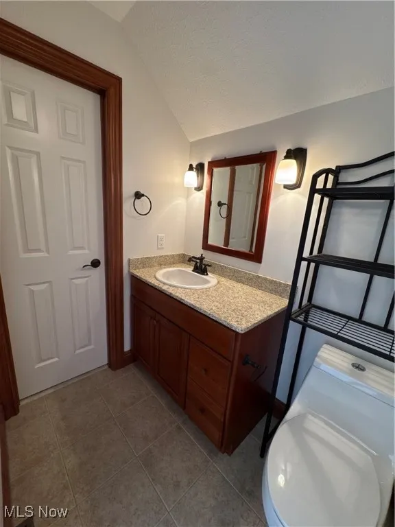 Bathroom with a textured ceiling, tile patterned floors, vaulted ceiling, and vanity