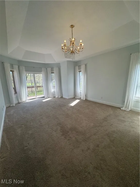Empty room with carpet floors, a chandelier, a wealth of natural light, and a raised ceiling