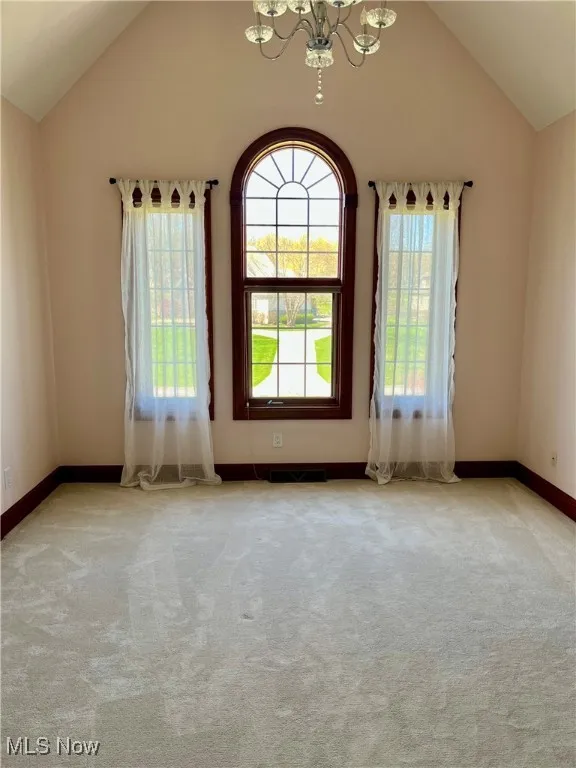 Carpeted empty room with visible vents, baseboards, a chandelier, and vaulted ceiling