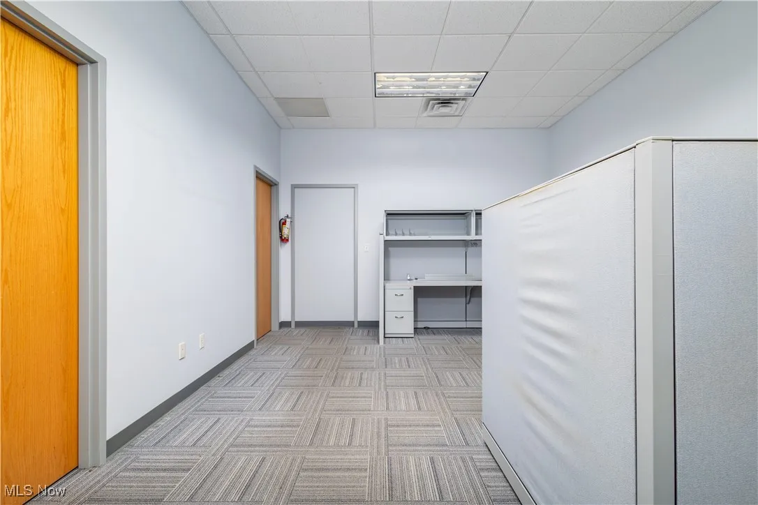 Hallway featuring light carpet and a paneled ceiling