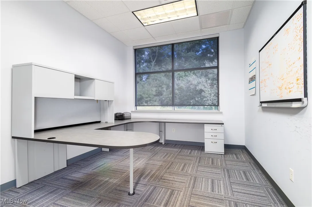 Unfurnished office with built in desk, a paneled ceiling, and dark carpet