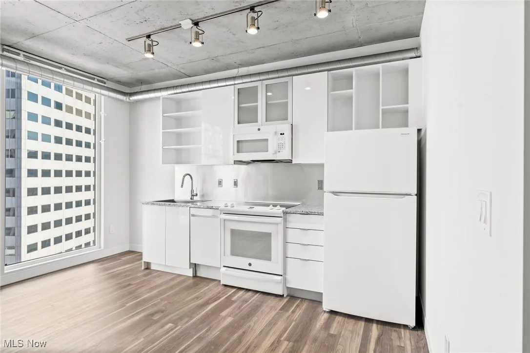 Kitchen with dark wood-type flooring, white cabinets, backsplash, white appliances, and sink
