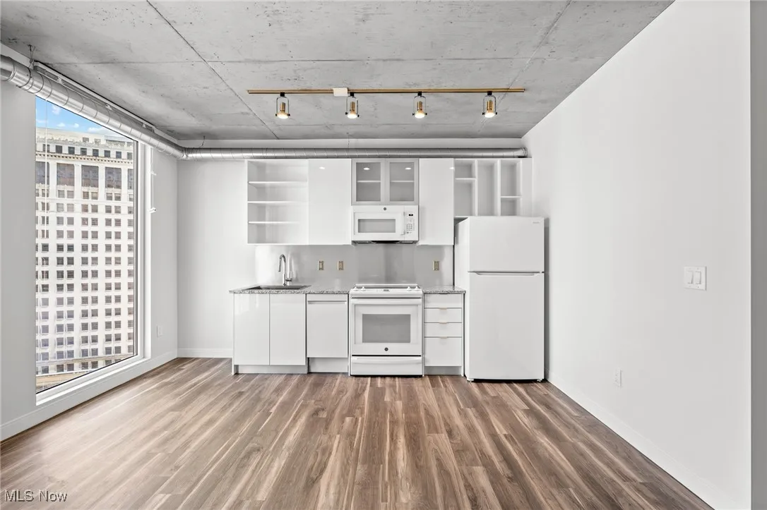 Kitchen with dark wood-type flooring, sink, white cabinetry, rail lighting, and white appliances