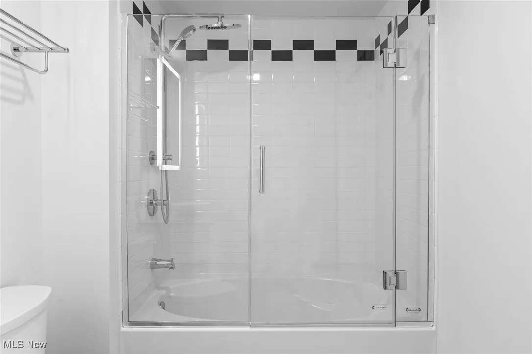 Bathroom with toilet and combined bath / shower with glass door