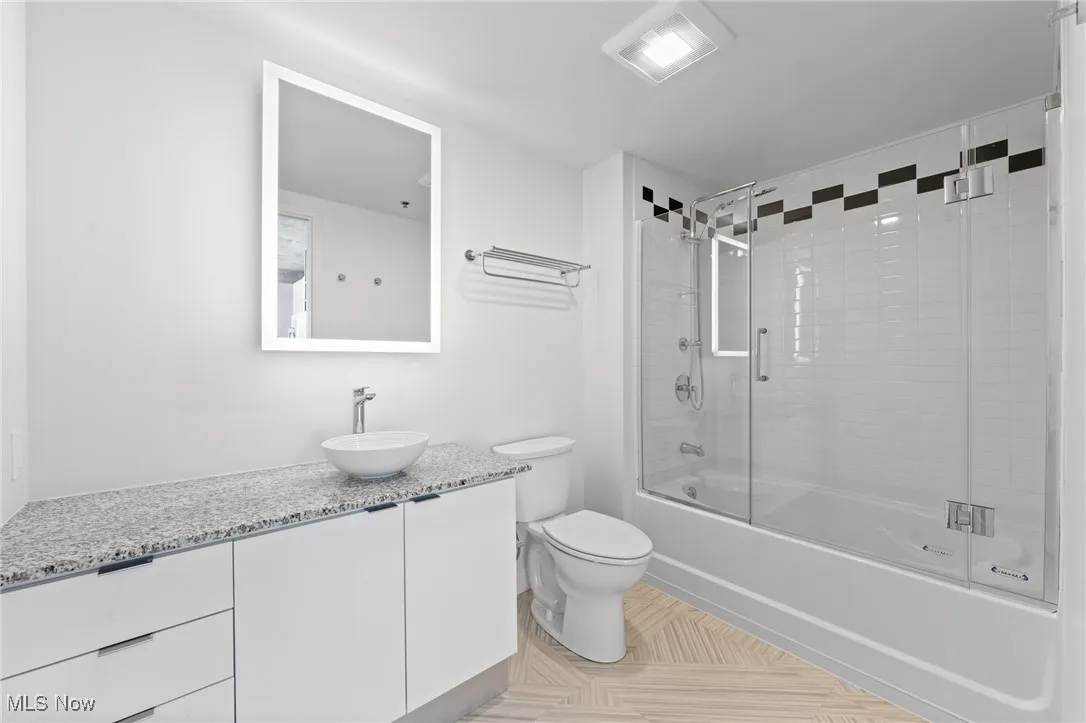 Full bathroom featuring combined bath / shower with glass door, vanity, toilet, and tile patterned flooring