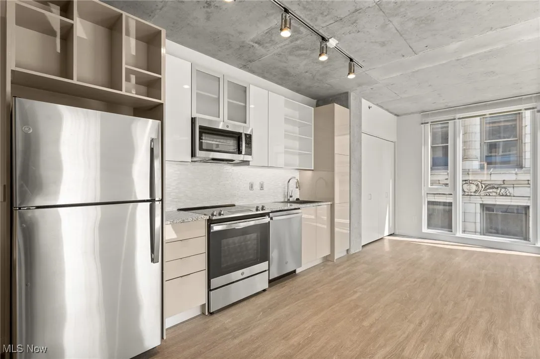 Kitchen featuring white cabinetry, light stone counters, backsplash, stainless steel appliances, and light wood-type flooring