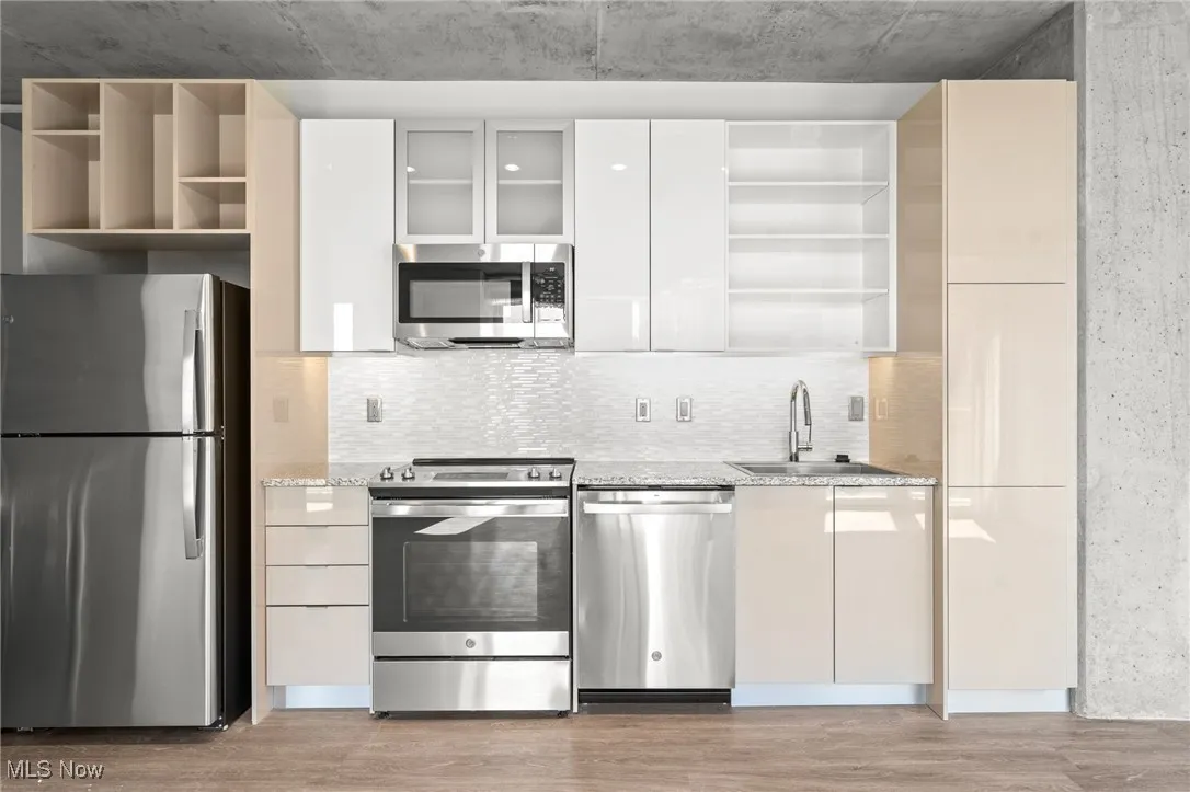Kitchen with white cabinetry, light stone countertops, stainless steel appliances, light wood-type flooring, and sink