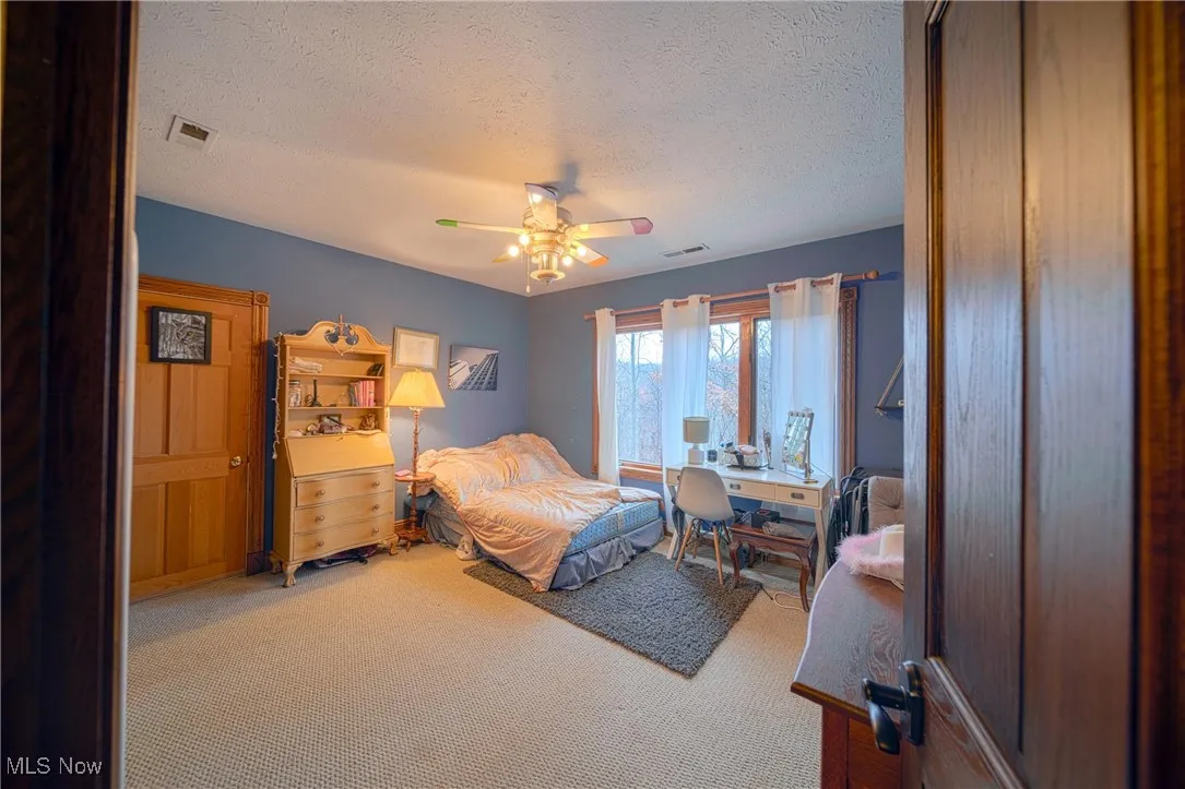 Carpeted bedroom featuring ceiling fan and a textured ceiling