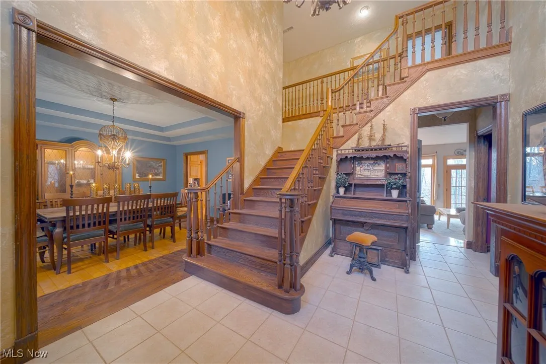 Staircase featuring a chandelier, a tray ceiling, light tile floors, and a high ceiling